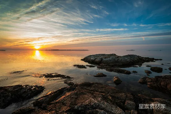 高清摄影 夕阳正在海洋上落下，前景中有岩石。