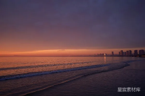 高清摄影 夕阳西下，海滩景色迷人，远处隐约可见一座城市。