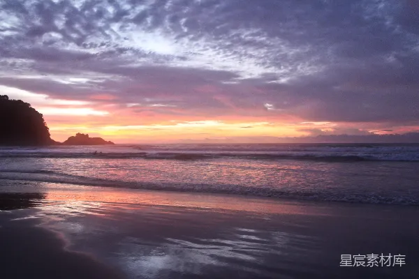 高清摄影 夕阳在海滩上落下，海浪拍打着岸边。