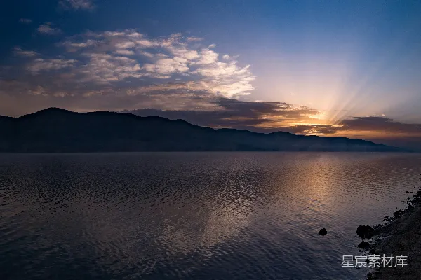 高清摄影 夕阳正洒落在湖面上，背景中是连绵的山脉。