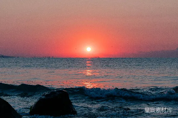 高清摄影 夕阳正从海平面上落下，前景中可以看到岩石。