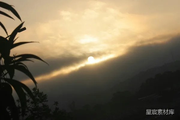 高清摄影 夕阳落在薄雾缭绕的群山之后，树木剪影清晰。