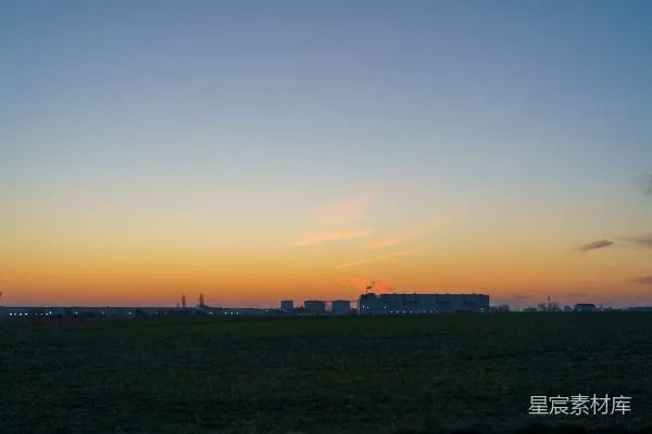 高清摄影 夕阳正在一片田野上落下，背景中有建筑物。