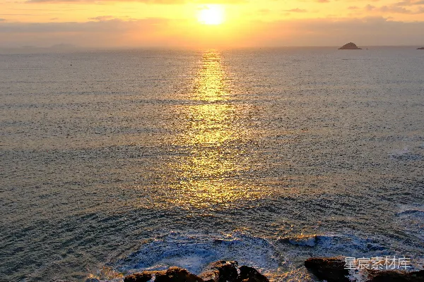 高清摄影 金色的夕阳洒在海洋上，岸边岩石嶙峋。