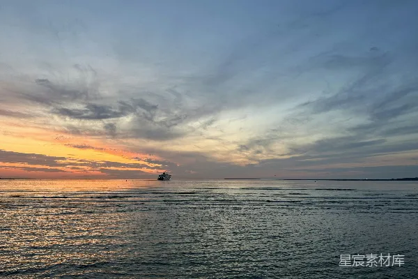 高清摄影 夕阳正映照着海面，远处有一艘小船。
