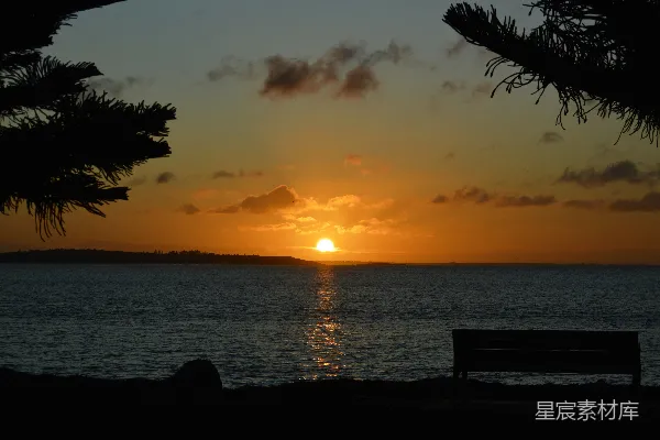 高清摄影 一张长椅坐落在海滩上，夕阳西下，夕阳映照其上。
