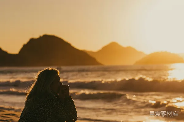 高清摄影 穿着黑白相间的连衣裙的女子坐在海滩上，夕阳西下。