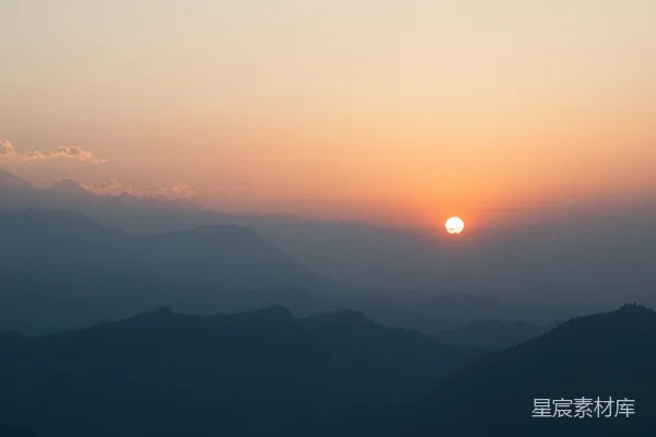 高清摄影 雾蒙蒙的蓝色山峦上初升的阳光，橙色的天空