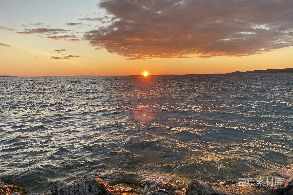 高清摄影 太阳正缓缓落下，海面的前景中有一些岩石。