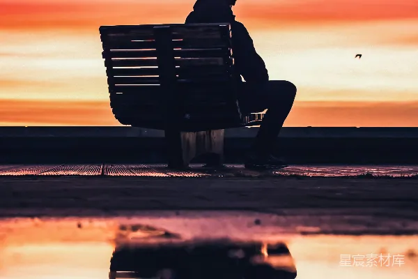 高清摄影 一个男人在海滩附近的长椅上坐着的剪影，夕阳西下。