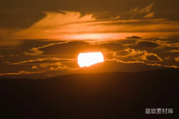 高清摄影 夕阳在山后落下，天空中飘着橙色的云。