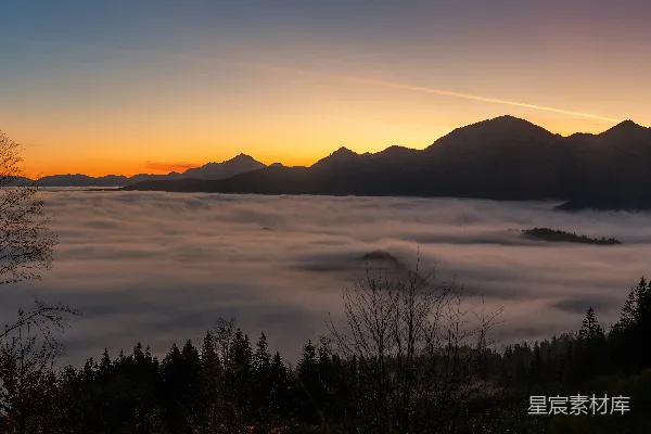 高清摄影 夕阳西下，云层和山脉笼罩在余晖之中。