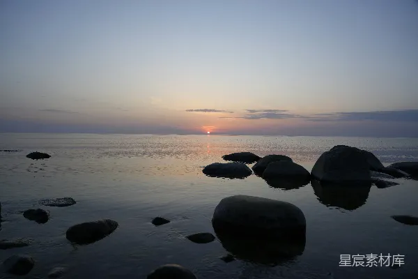 高清摄影 平静的海面上夕阳西下，前景中有岩石。