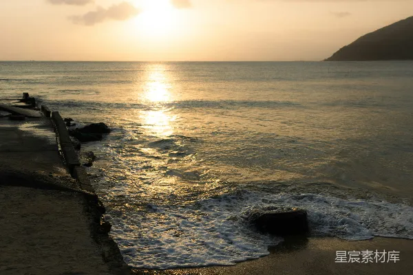 高清摄影 金色的夕阳洒在海洋上，波浪轻轻拍打着岸边。