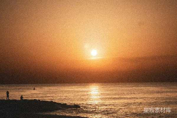 高清摄影 夕阳映照着平静的海洋，岸边有人在散步。