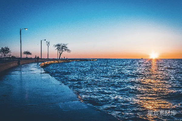 高清摄影 两个人在水边的街道上散步，正值夕阳西下的黄金时刻。