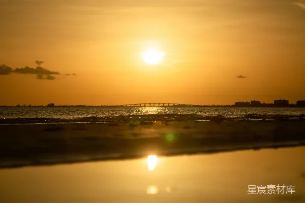 高清摄影 太阳正在海上落下，远处有一座桥。