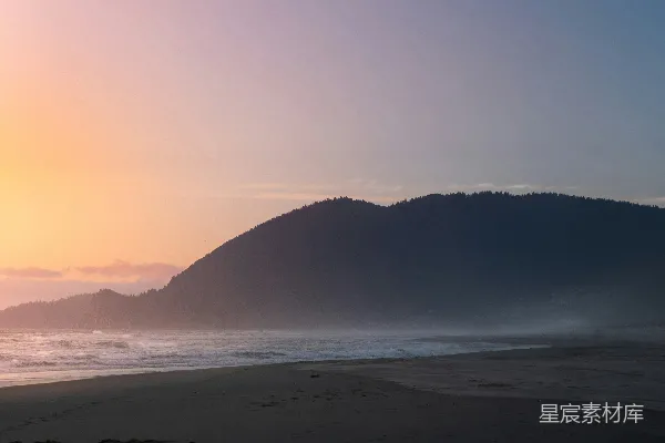 高清摄影 太阳正落在这片海滩上，背景是连绵的山脉。
