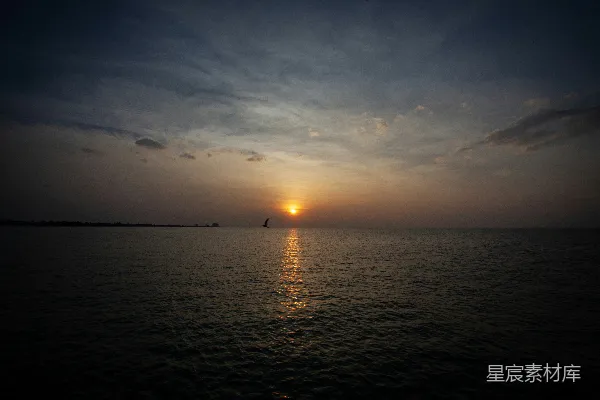 高清摄影 夕阳正缓缓落下，海面上一艘帆船在远处漂浮。