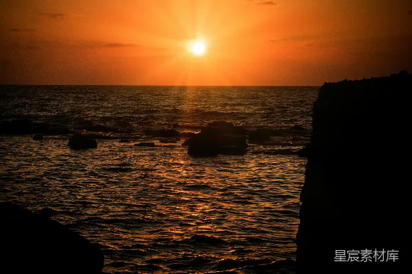 高清摄影 夕阳正缓缓落下，海面的岩石在前景中显得格外突出。
