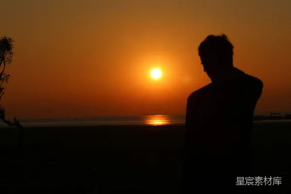 高清摄影 一个男人站在海滩上，夕阳西下。