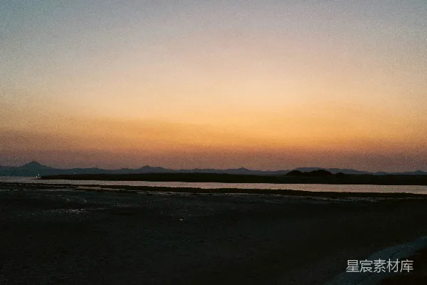 高清摄影 夕阳映照在水面上，背景中有连绵的山脉。