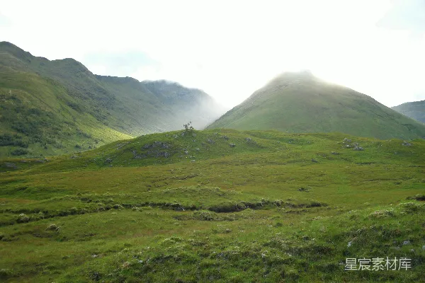 高清摄影 一座长满草的小山，背景中有更高的小山。