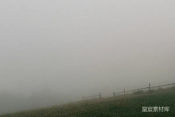 高清摄影 被浓雾笼罩的草地小丘，旁边有一道木栅栏。