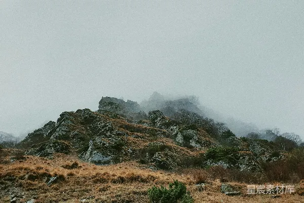 高清摄影 白天的白色天空下，山坡上有一片棕色的草地。