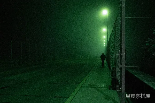 高清摄影 夜晚，一位穿着黑色夹克的男子在人行道上行走。
