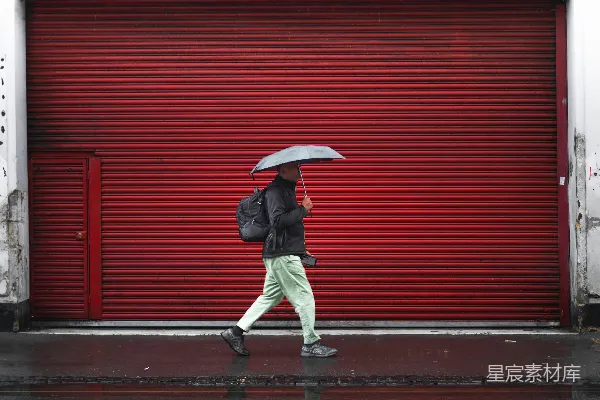 高清摄影 穿黑色夹克和灰色裤子的男人打着伞走在人行道上。