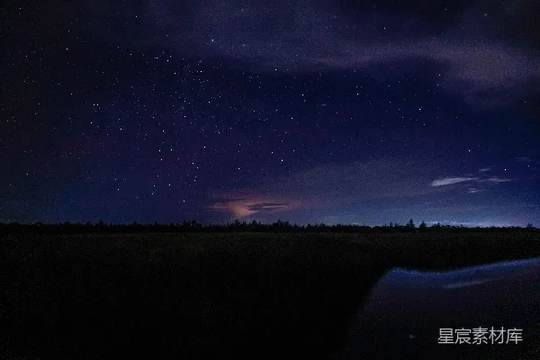 高清摄影 夜空中的星星和云彩笼罩在一片田野上方。