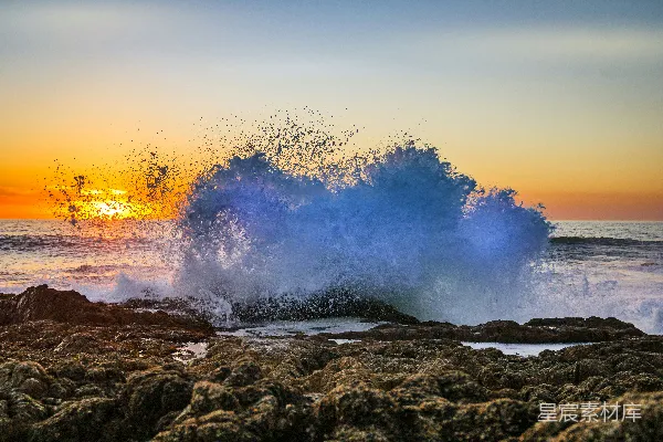 高清摄影 夕阳下，海浪拍打在岩石岸边。
