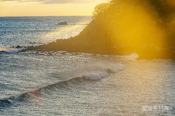 高清摄影 夕阳下，海浪拍打着被阳光照亮的岩石海岸线。