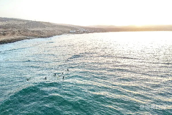 高清摄影 冲浪者在夕阳下沿着沙滩海岸线冲浪。