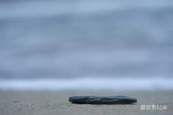 高清摄影 一块黑色的石头静静地躺在沙滩上。