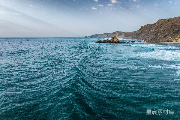 高清摄影 湛蓝的海洋波涛中，有冲浪者和岩石海岸线。