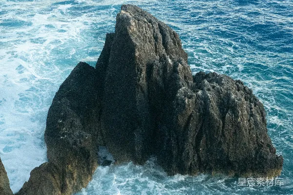 高清摄影 海洋中的尖锐岩石，海浪拍打在岩石上。