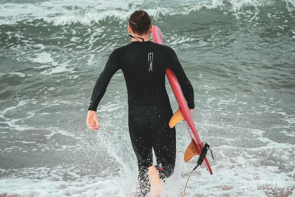 高清摄影 一个穿着潜水服的男人扛着冲浪板走向海洋。