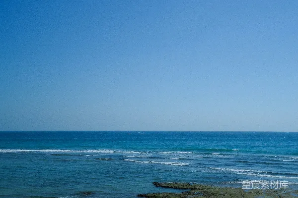 高清摄影 晴朗的蓝天映衬着平静的海洋，海岸上分布着岩石。