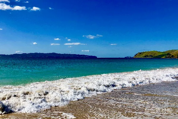 高清摄影 海浪拍打着沙滩，蓝色的天空下。