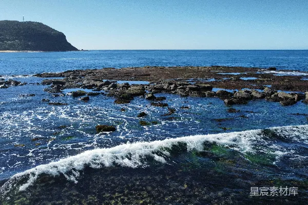 高清摄影 海浪拍打着岩石海岸，远处有一座海岬。