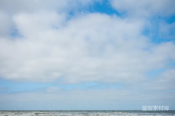 高清摄影 沙滩上有海浪，天空是阴云密布的蓝色。