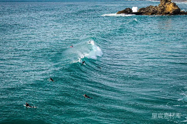 高清摄影 冲浪者在岩石海岸线附近的海浪上冲浪。