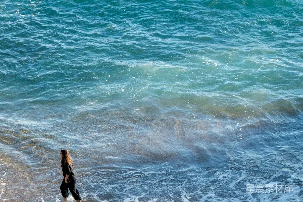 高清摄影 一个女人在浅蓝色的海水中走在沙滩上。
