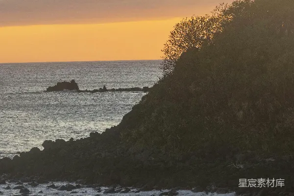 高清摄影 夕阳洒在岩石海岸上，海浪拍打着岸边。