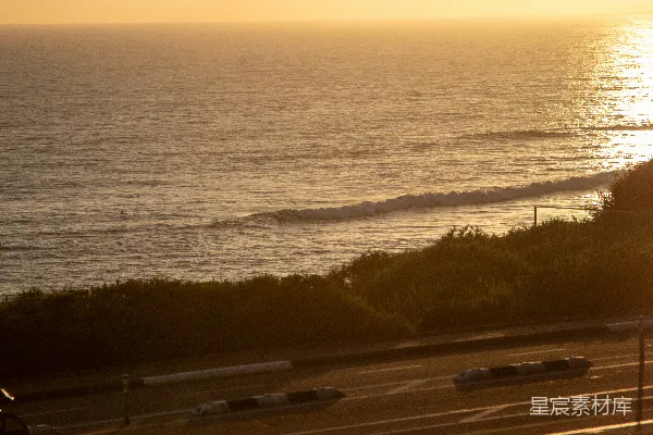 高清摄影 金色的夕阳洒在海洋上，海浪轻拍岸边的道路。