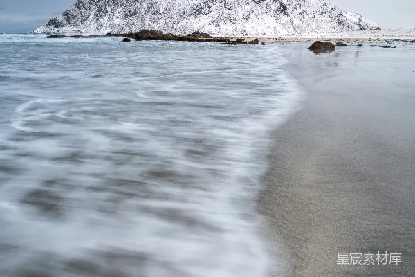 高清摄影 一座被雪覆盖的山峦俯瞰着海滩，海浪模糊不清。
