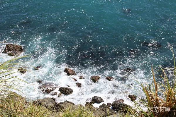 高清摄影 碧蓝的海浪拍打着草地悬崖下的岩石。