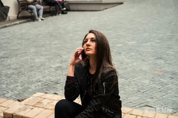 高清摄影 穿着黑色皮夹克的女人坐在白天的棕色砖地上。